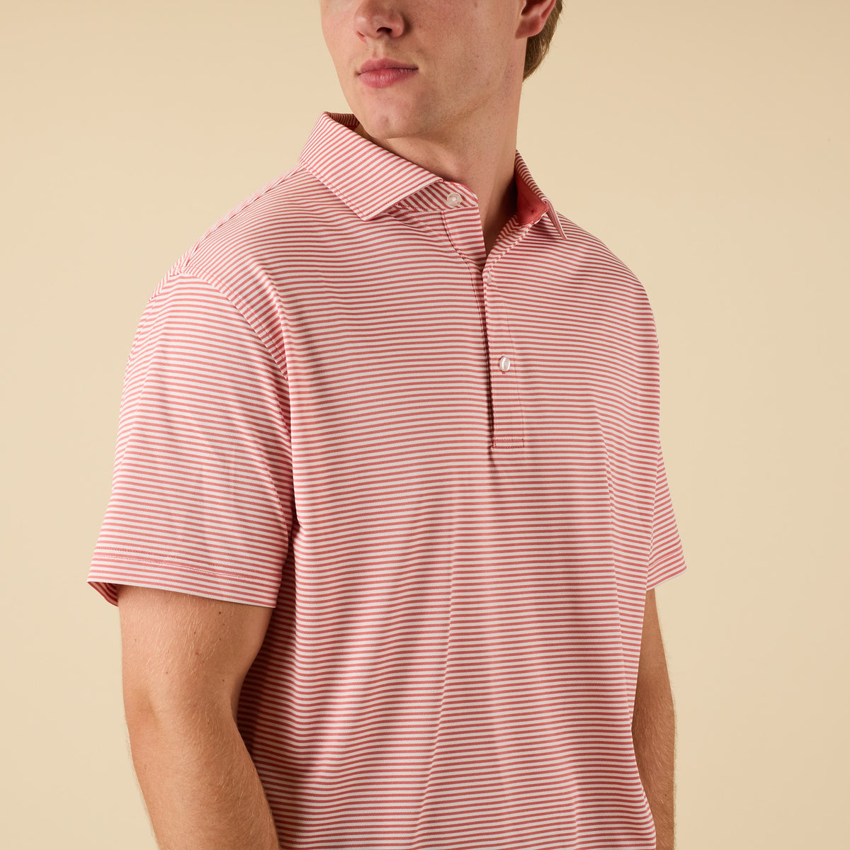 Man wearing a pink striped polo on a beige background.