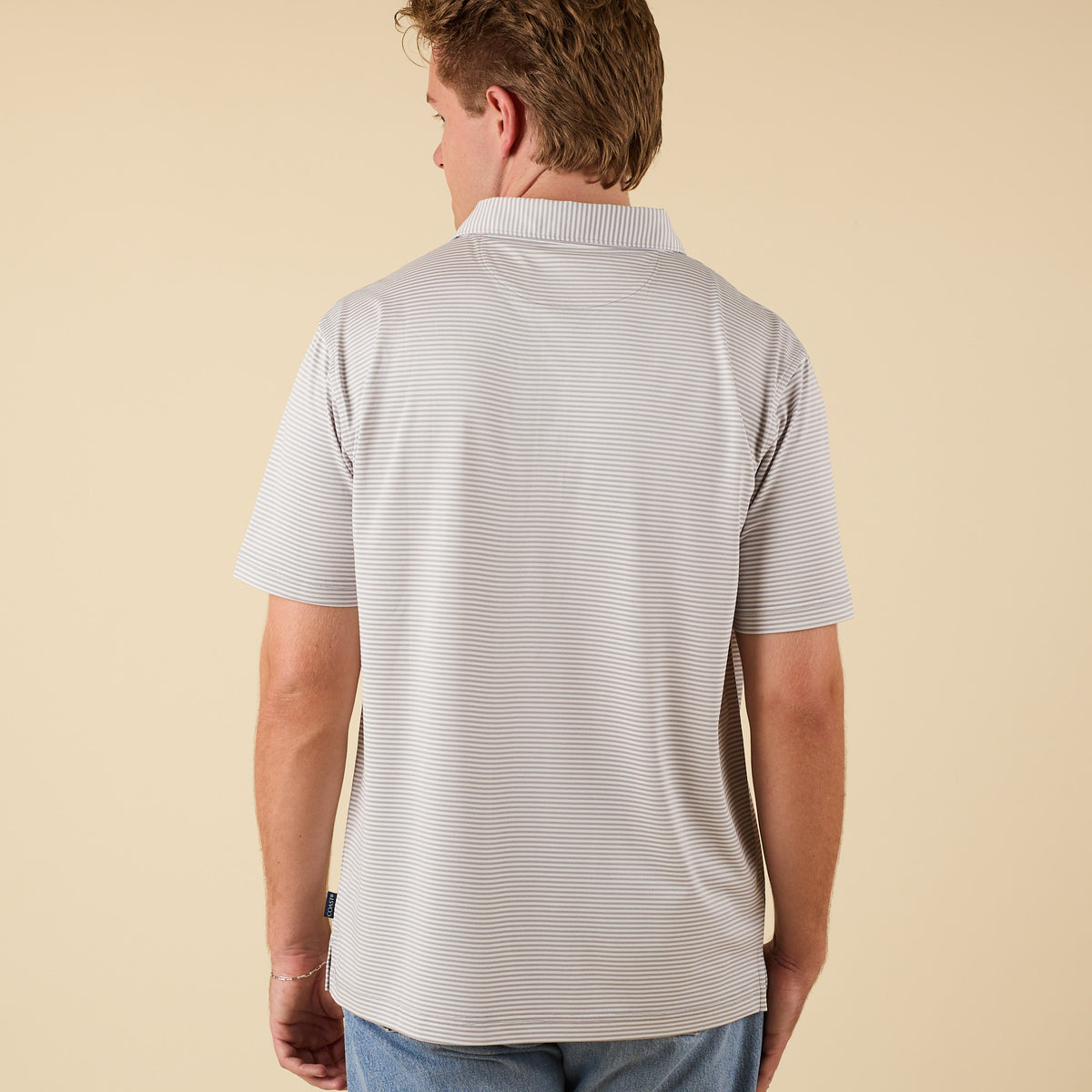 Man wearing a light gray striped polo shirt on a beige background