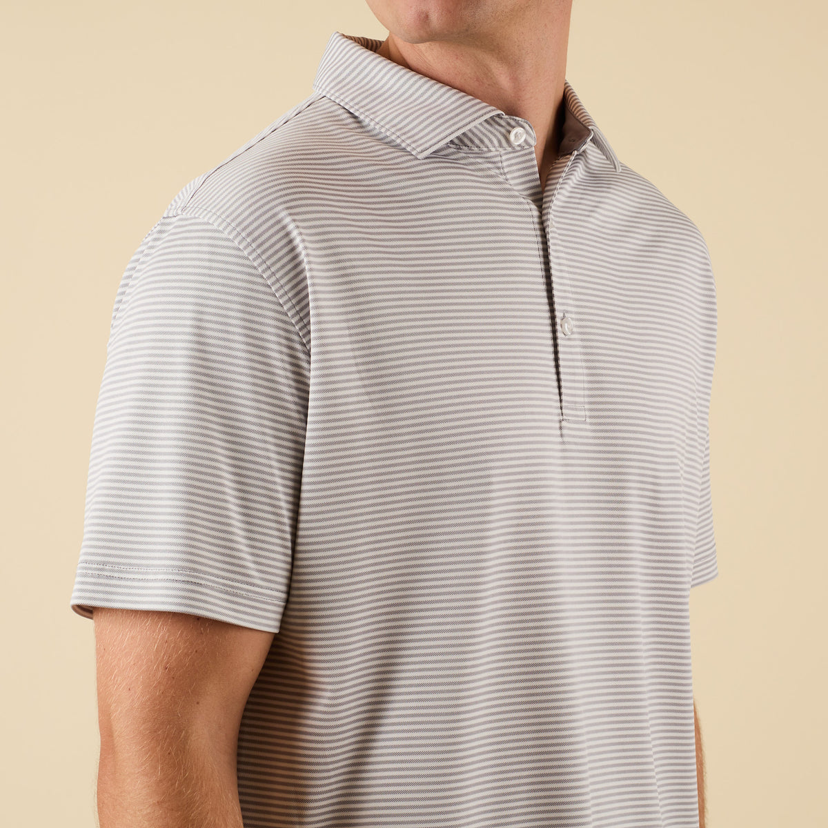 Man wearing a gray striped polo shirt against a beige background