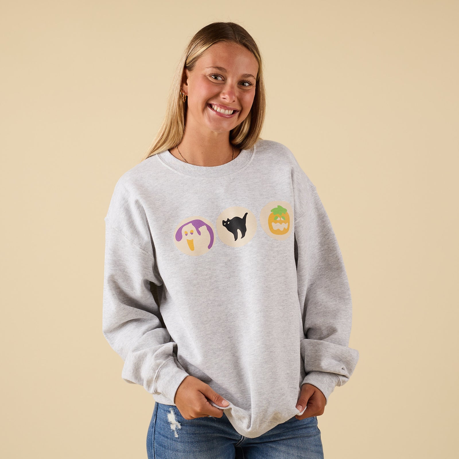 Front view of model wearing light grey sweatshirt with spooky cookie Halloween graphics.