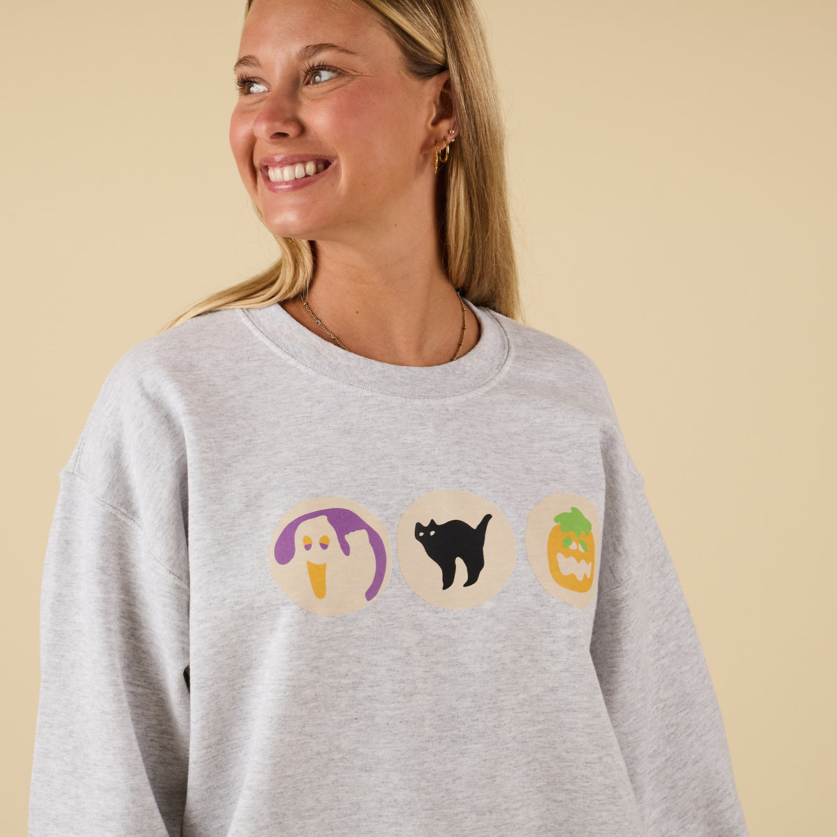 Close-up of light grey sweatshirt with ghost, black cat, and jack-o’-lantern cookie graphics across chest.
