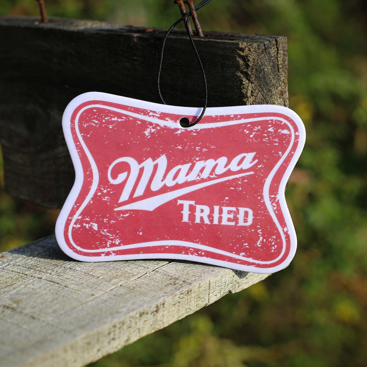 Scent South red distressed air freshener with “Mama Tried” text in white script, hanging outdoors.