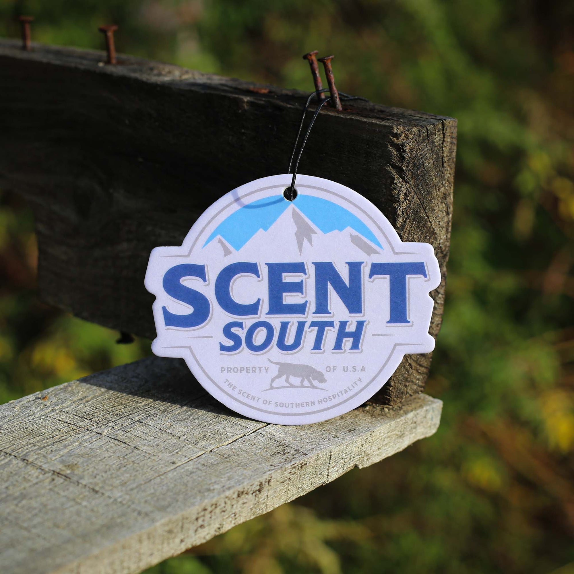 Scent South air freshener with blue mountain logo and “Scent South” branding in bold letters, hanging from a string.