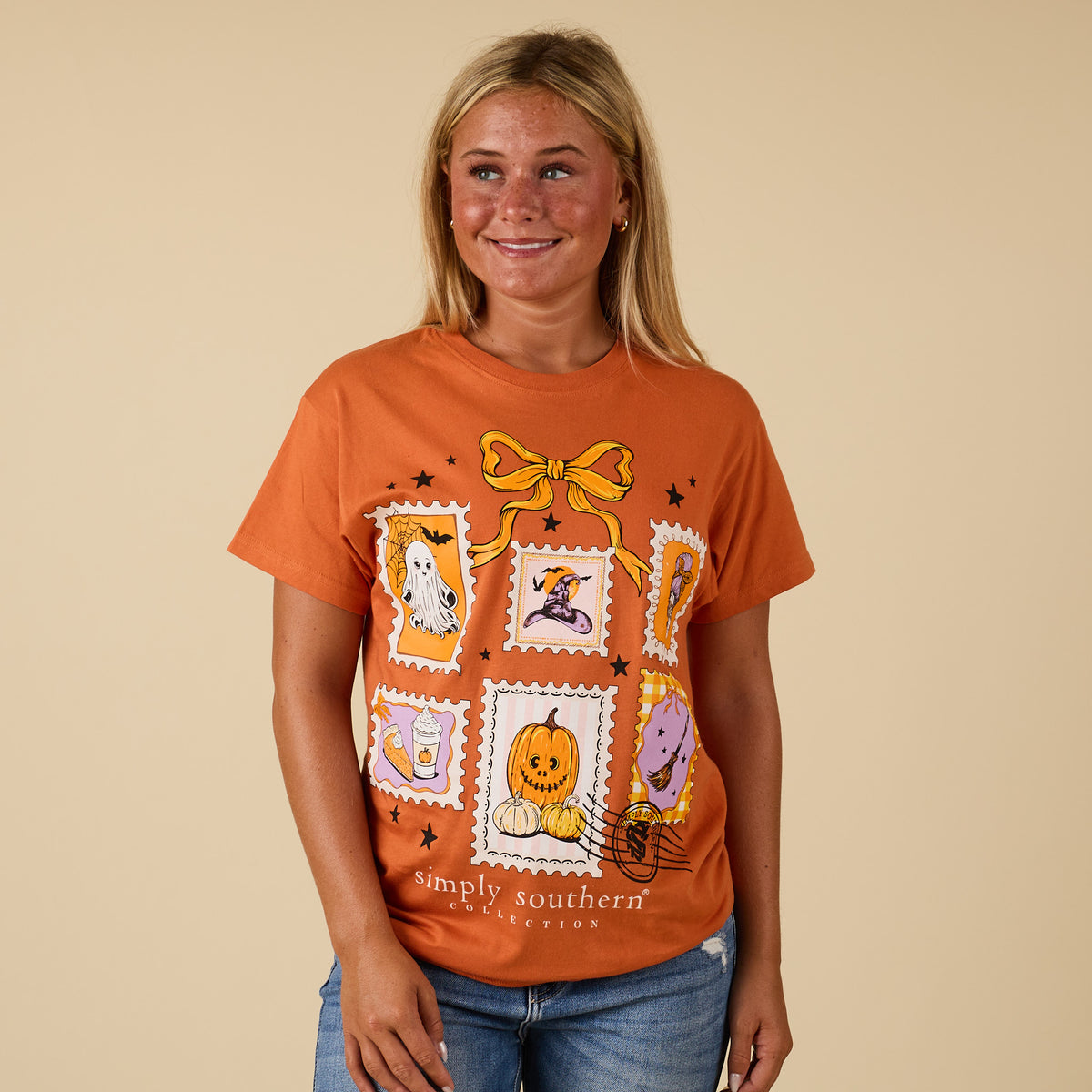Caramel orange Simply Southern short sleeve tee with Halloween stamp graphics including ghost, pumpkin, witch hat, broom, and fall drink, shown on model.