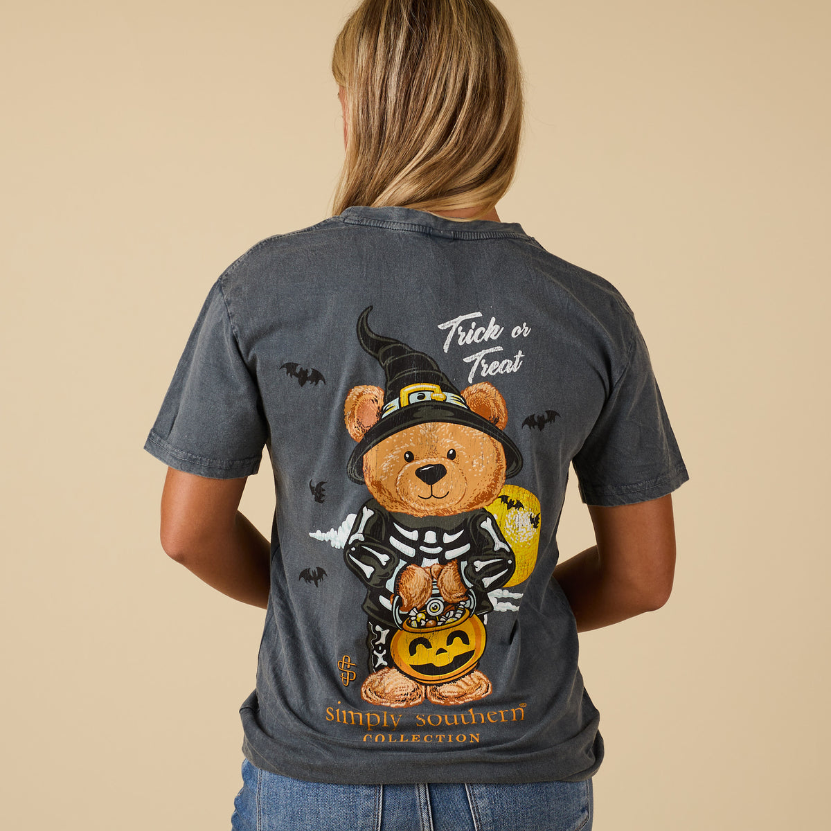 Back of washed coal Simply Southern short sleeve tee with teddy bear in skeleton costume and witch hat holding pumpkin candy bucket, “Trick or Treat” text above.