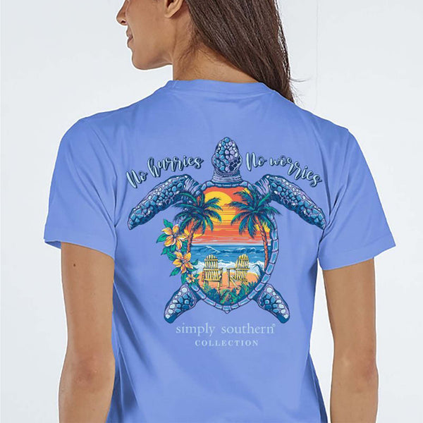 Periwinkle short sleeve shirt with the phrase 'No hurries no worries." A turtle with a sunset beach scene on the shell. Tropical flowers around. Simply Southern logo below and on left chest.