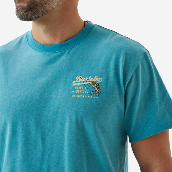 Close-up of the chest graphic on a teal short sleeve Burlebo t-shirt featuring “Bait + Rigs Austin, Texas USA” text and a largemouth bass illustration.