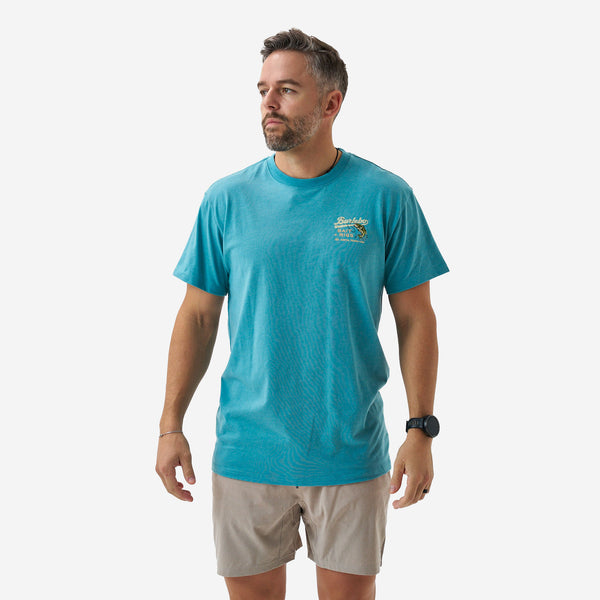 Male model wearing a teal short sleeve Burlebo graphic t-shirt with small chest logo, paired with khaki shorts, shown standing against a white background.