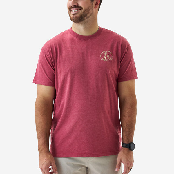 Male model wearing a heather red short sleeve Burlebo t-shirt with a small “Burlebo Outdoors Austin, Texas Since ’15” duck logo on the chest.