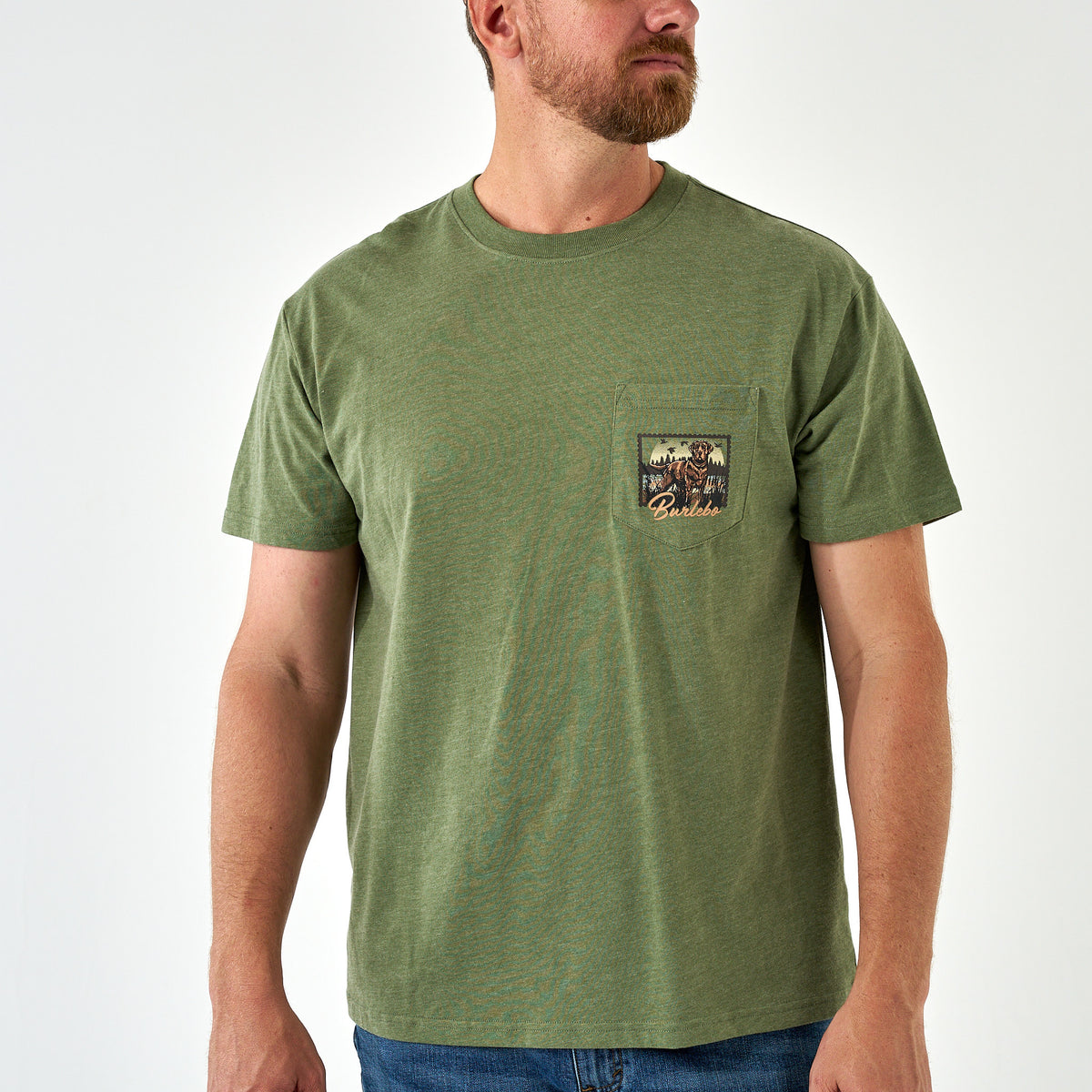 Man wearing an olive green Burlebo short sleeve t-shirt with a small chest pocket featuring a hunting dog and outdoor scene graphic.