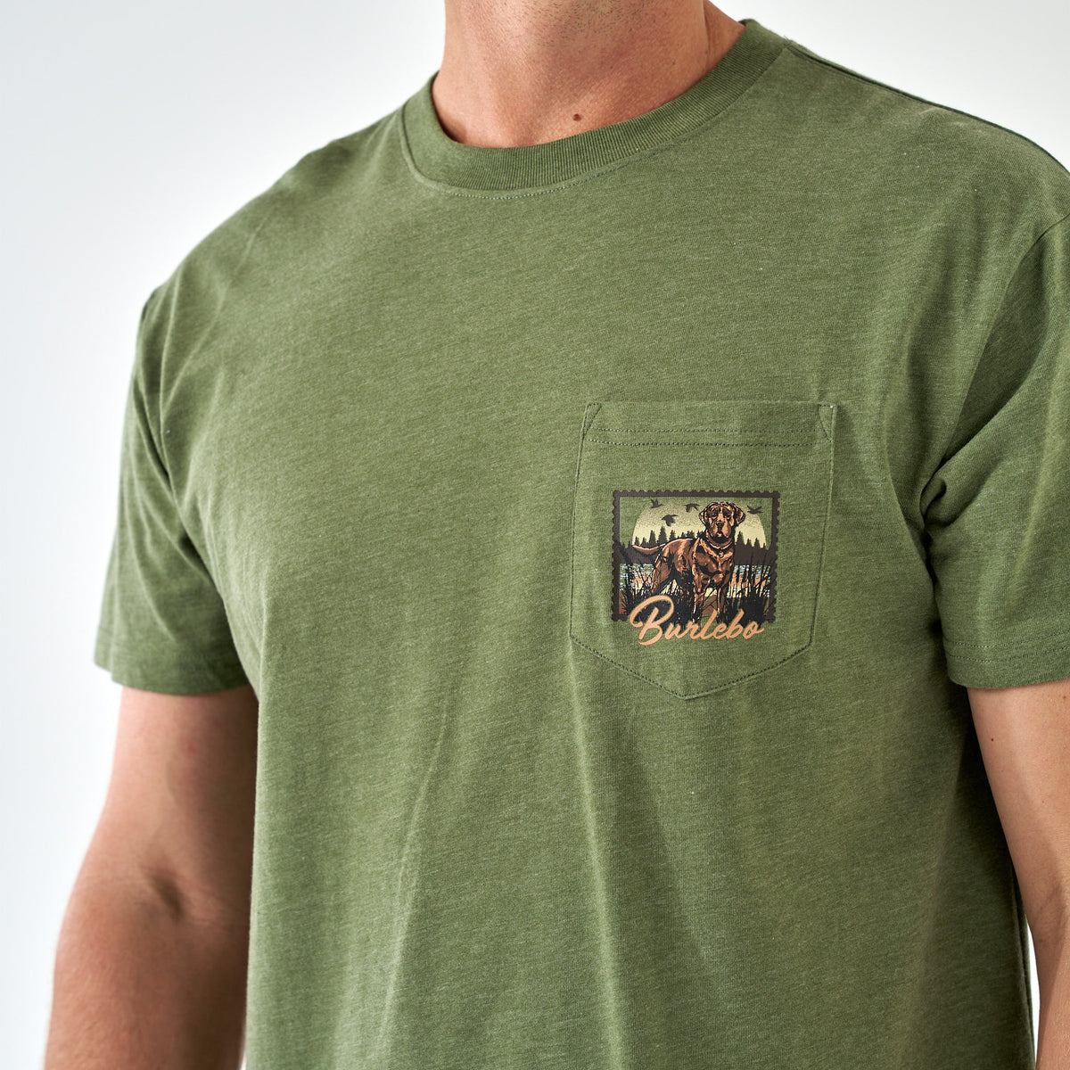 Close-up of chest pocket on olive green Burlebo t-shirt with hunting dog and forest graphic.