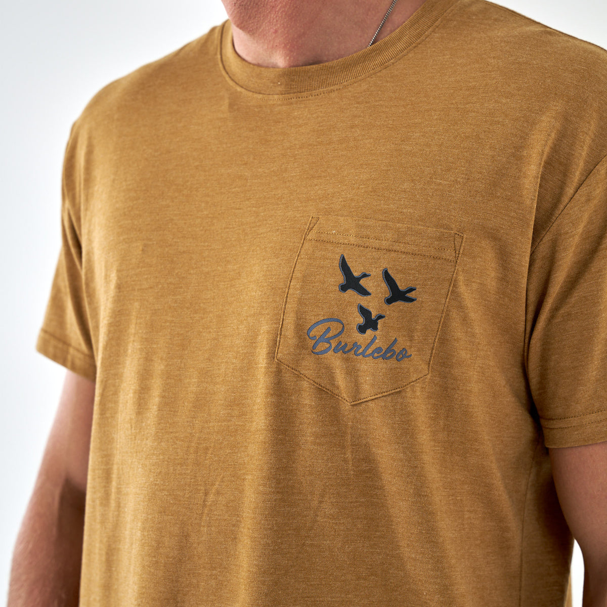 Close-up of pocket with three flying ducks and Burlebo logo on light brown tee.