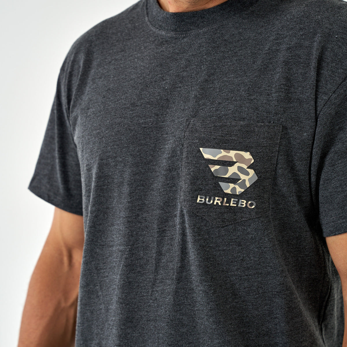 Close-up of the chest pocket on a dark charcoal t-shirt with a light brown camo Burlebo logo.