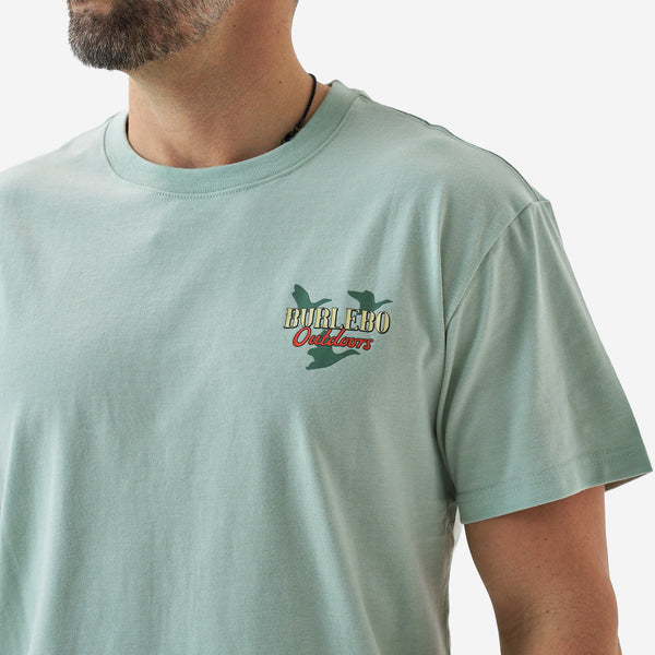 Close-up of the chest graphic on a sage green short sleeve Burlebo t-shirt showing “Burlebo Outdoors” text with duck silhouettes above.