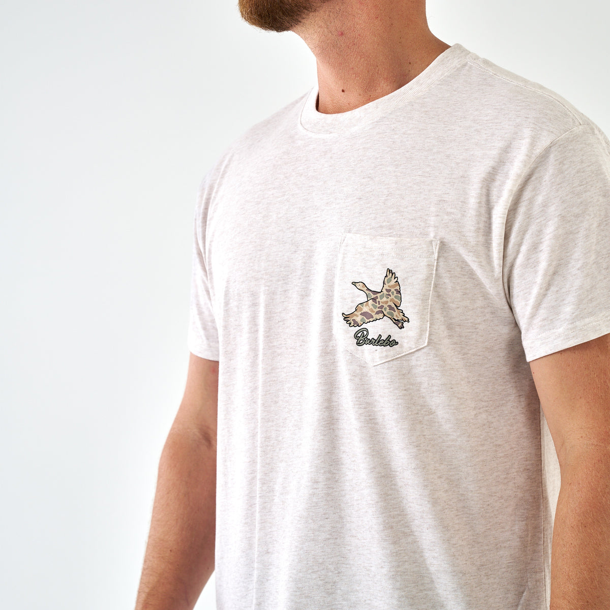 Light oat short sleeve t-shirt with camo duck graphic on chest pocket and "Burlebo" text, partial side view.