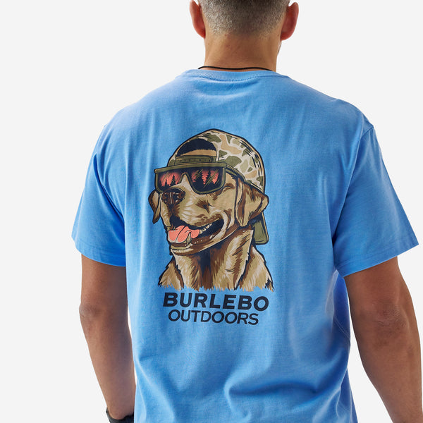 Close-up of the back graphic on a bright blue Burlebo t-shirt showing a dog wearing sunglasses and a camouflage hat above “Burlebo Outdoors” lettering.
