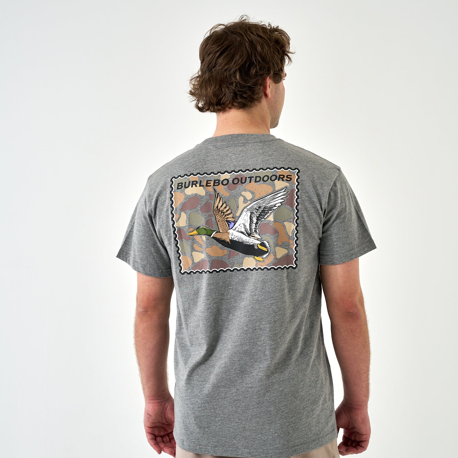 Model wearing dark heather gray Burlebo Outdoors t-shirt showing back duck stamp graphic.