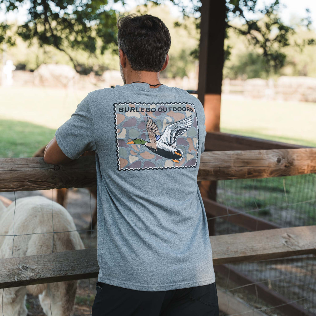 Back view of dark heather gray short sleeve t-shirt with large Burlebo Outdoors flying duck stamp graphic. 