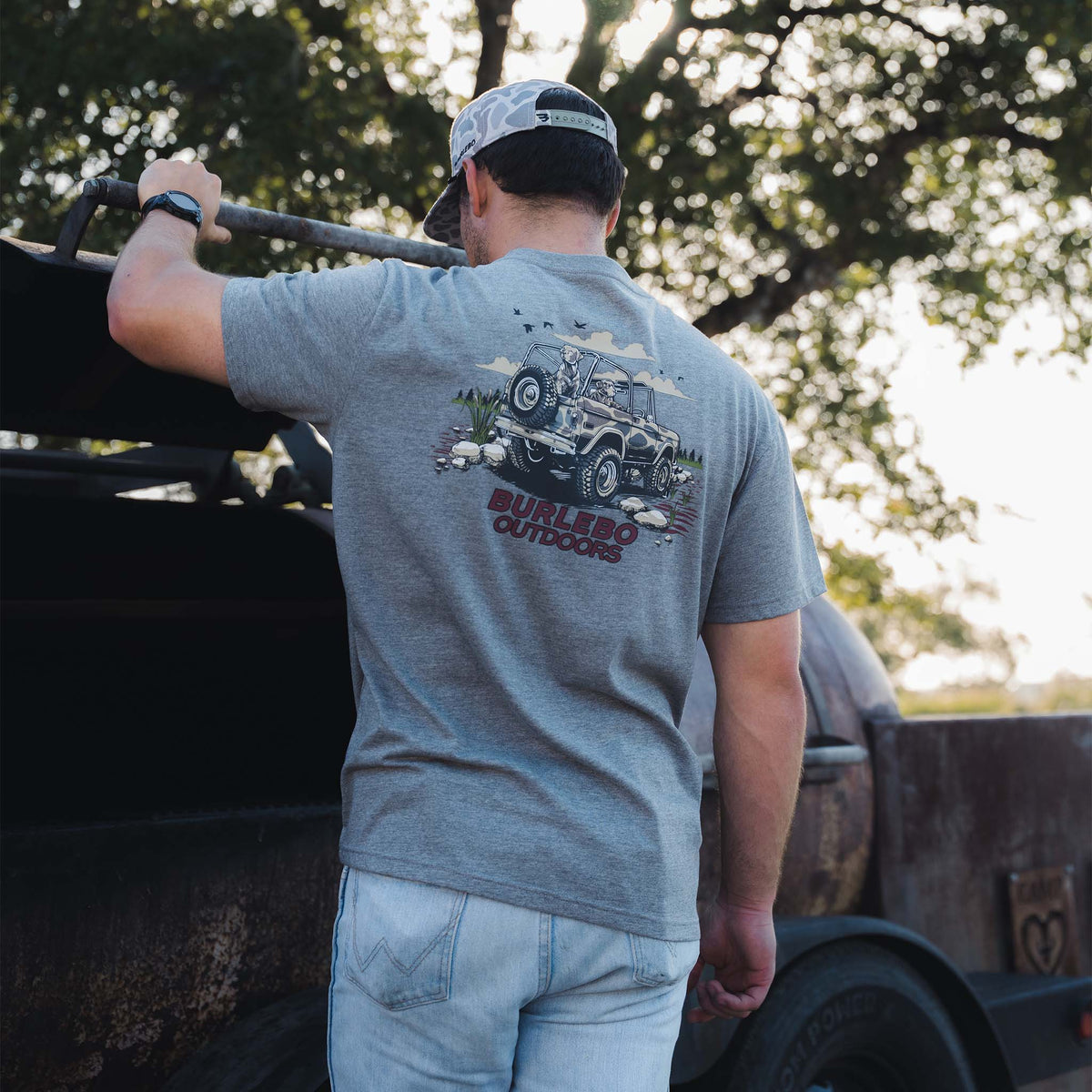 Man wearing gray t-shirt with large jeep and dogs graphic on back, “Burlebo Outdoors” text.