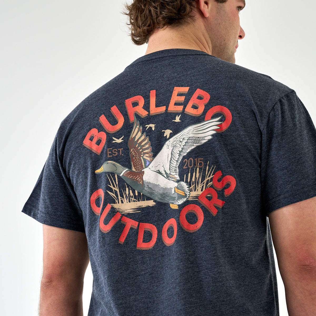 Close-up of large flying duck graphic with “Burlebo Outdoors” red text on back of navy t-shirt.
