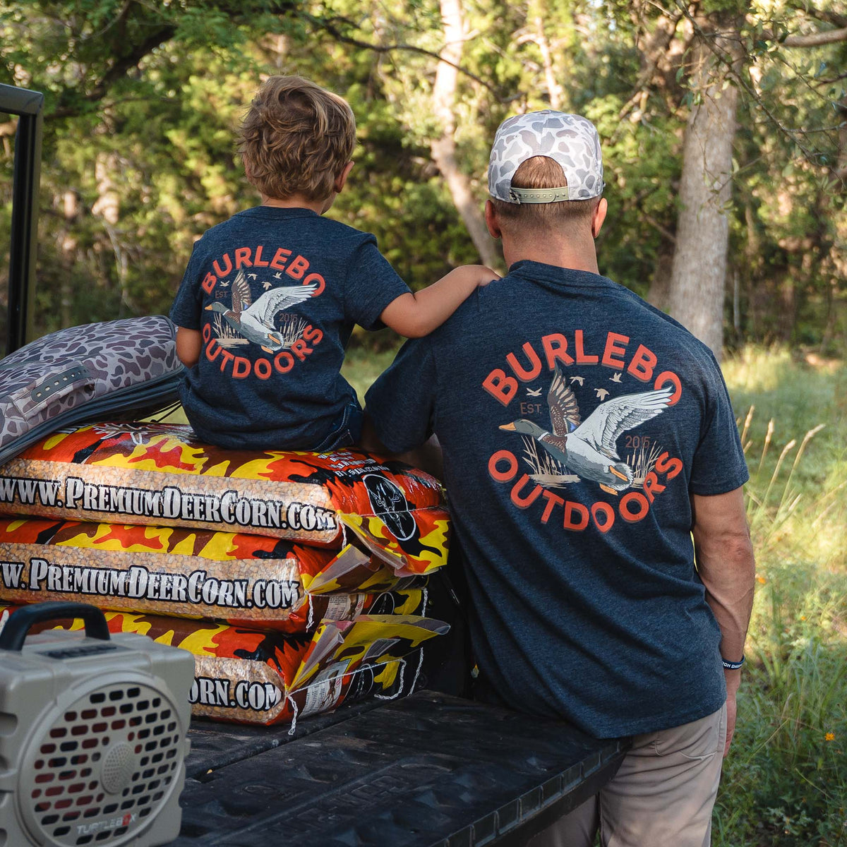Man and child in matching navy Burlebo Outdoors t-shirts with large duck graphic and red text on back.