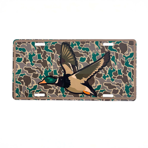 Scent South Mallard Camo License Plate, metal.
Rectangular metal license plate with a camouflage background in shades of green, brown, and tan, featuring a graphic of a flying mallard duck with outstretched wings in the center. The plate includes four pre-drilled mounting holes.