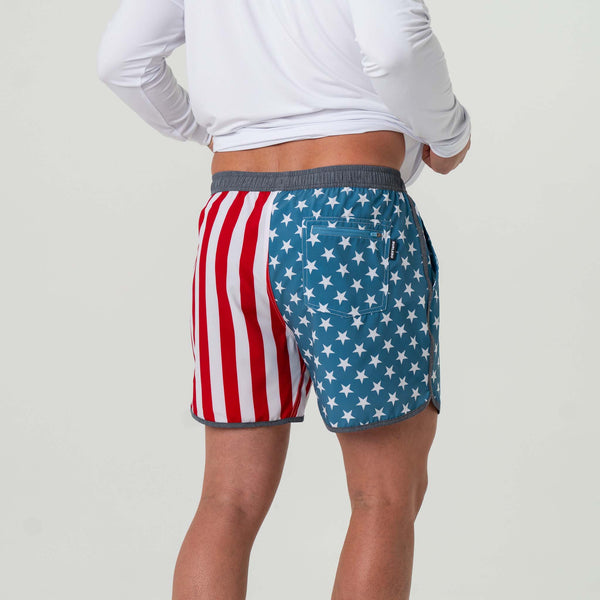 Burlebo Men's Swim Trunks in Throwback USA. Sizes S-XXL. Rear view of a man modeling the trunks, showing contrasting red stripes and white stars on blue with a back pocket.