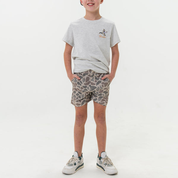 Child wearing a gray t-shirt and patterned shorts on a white background