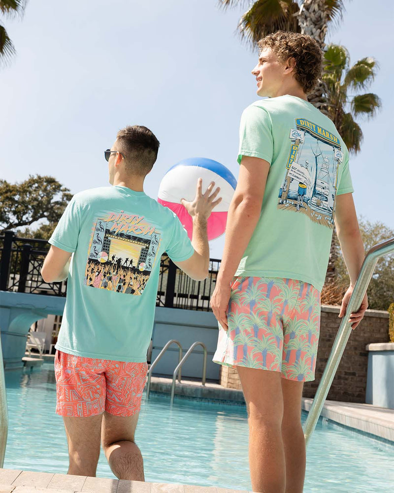 Two men wearing graphic t-shirts and patterned swim shorts standing poolside with beach ball.