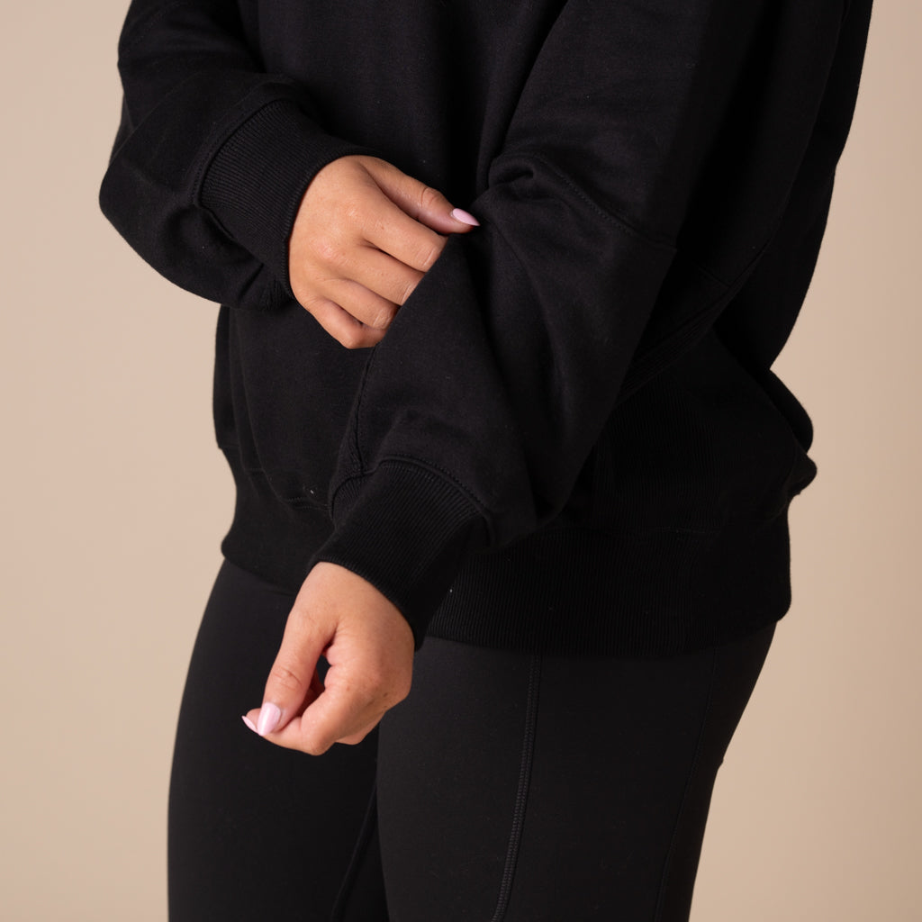 Person wearing a black sweatshirt and leggings on a beige background