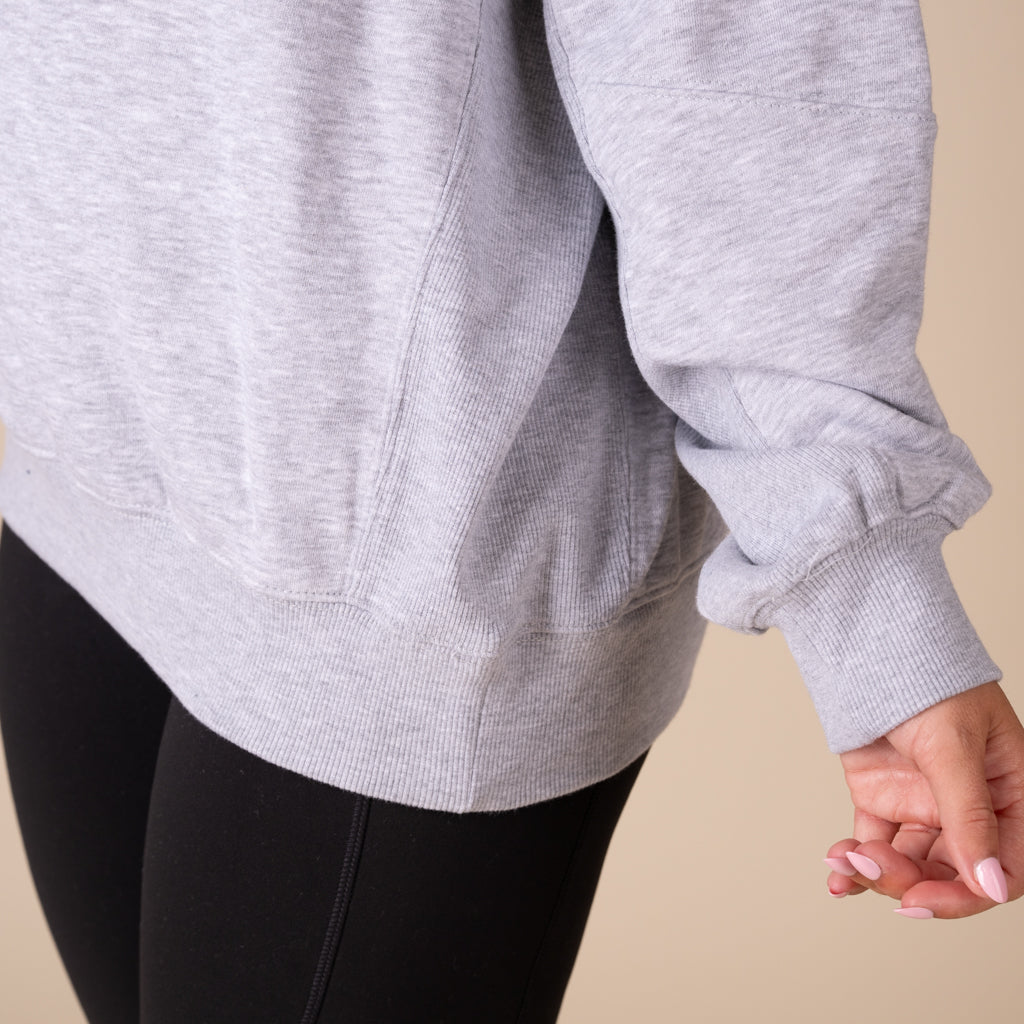 Person wearing a gray sweatshirt and black leggings on a beige background