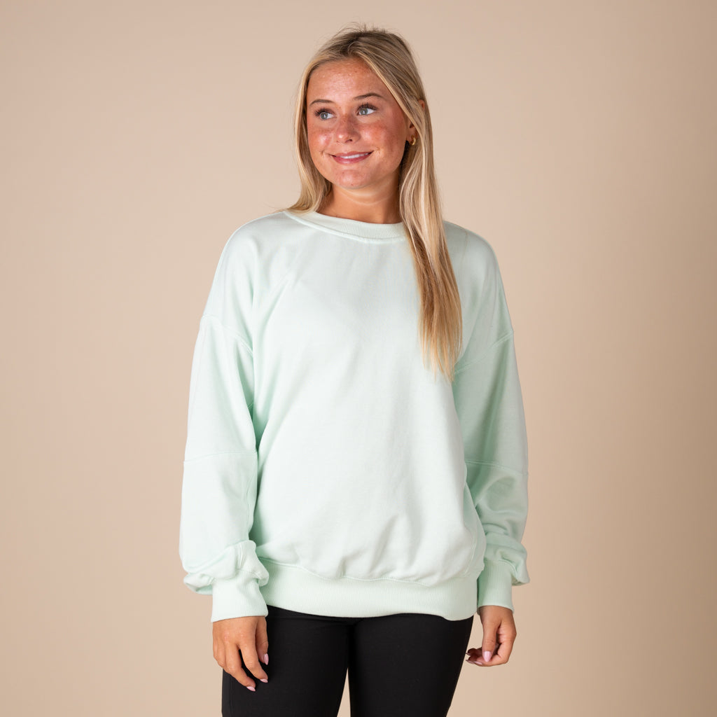 Woman wearing a light green sweatshirt against a beige background