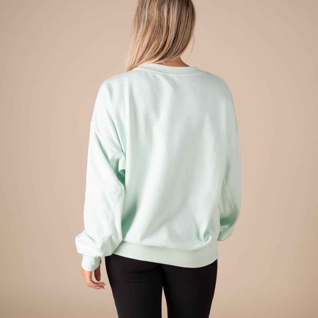 Person wearing a light green sweatshirt on a beige background