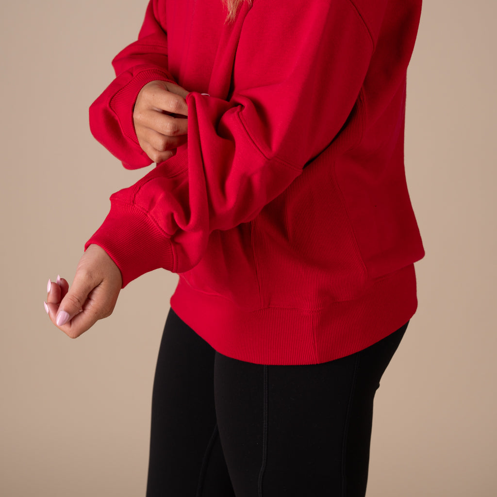 Person wearing a red sweatshirt and black pants on a beige background