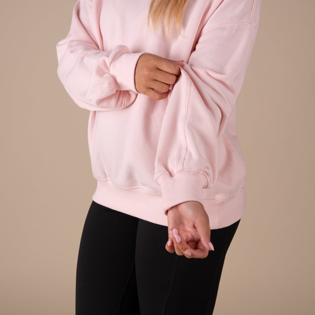 Person wearing a pink sweatshirt and black pants on a beige background