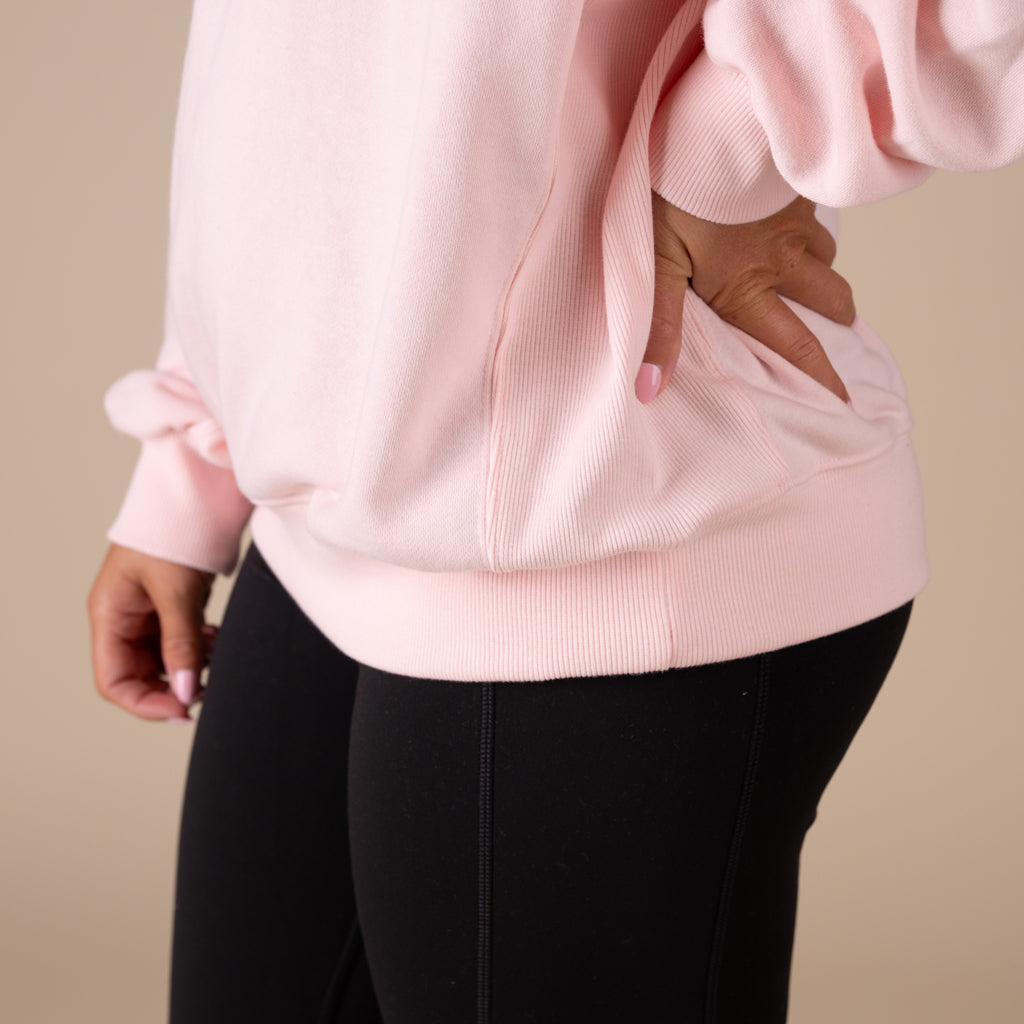 Person wearing a light pink sweatshirt and black pants on a beige background