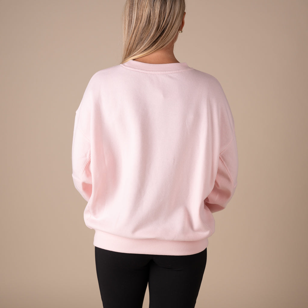 Person wearing a light pink sweatshirt and black pants on a beige background