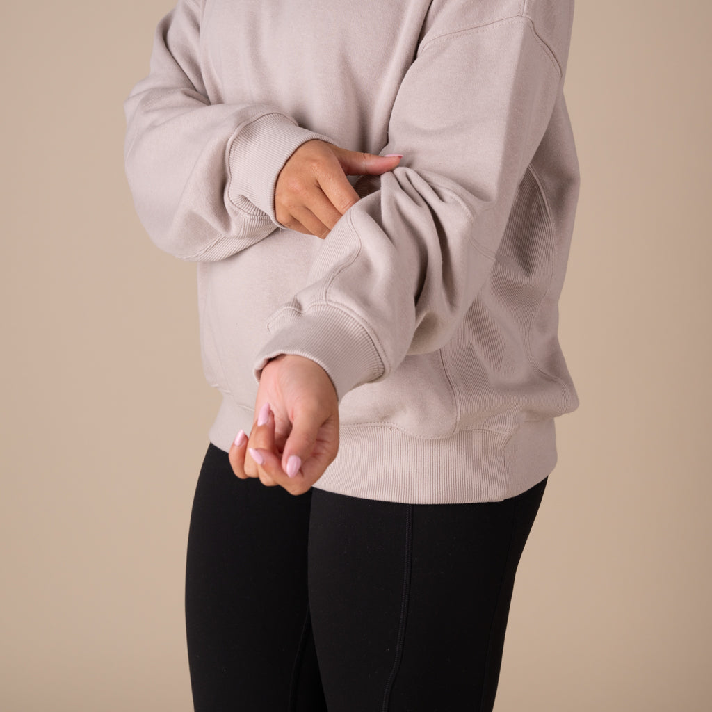 Person wearing a beige swestshirt and black pants on a beige background