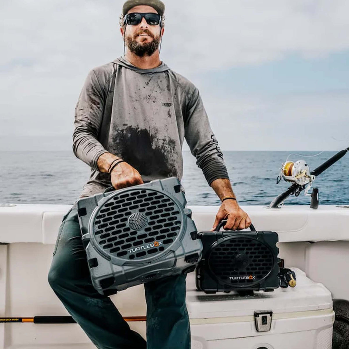 Lifestyle image of man holding Turtlebox Grande Speaker in Grey and Turtlbox Gen 3 Grey speaker for size comparison