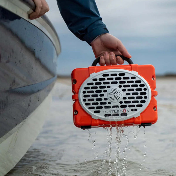Man holding an orange turtlebox off the side of a boat to show that the speaker is waterproof.
