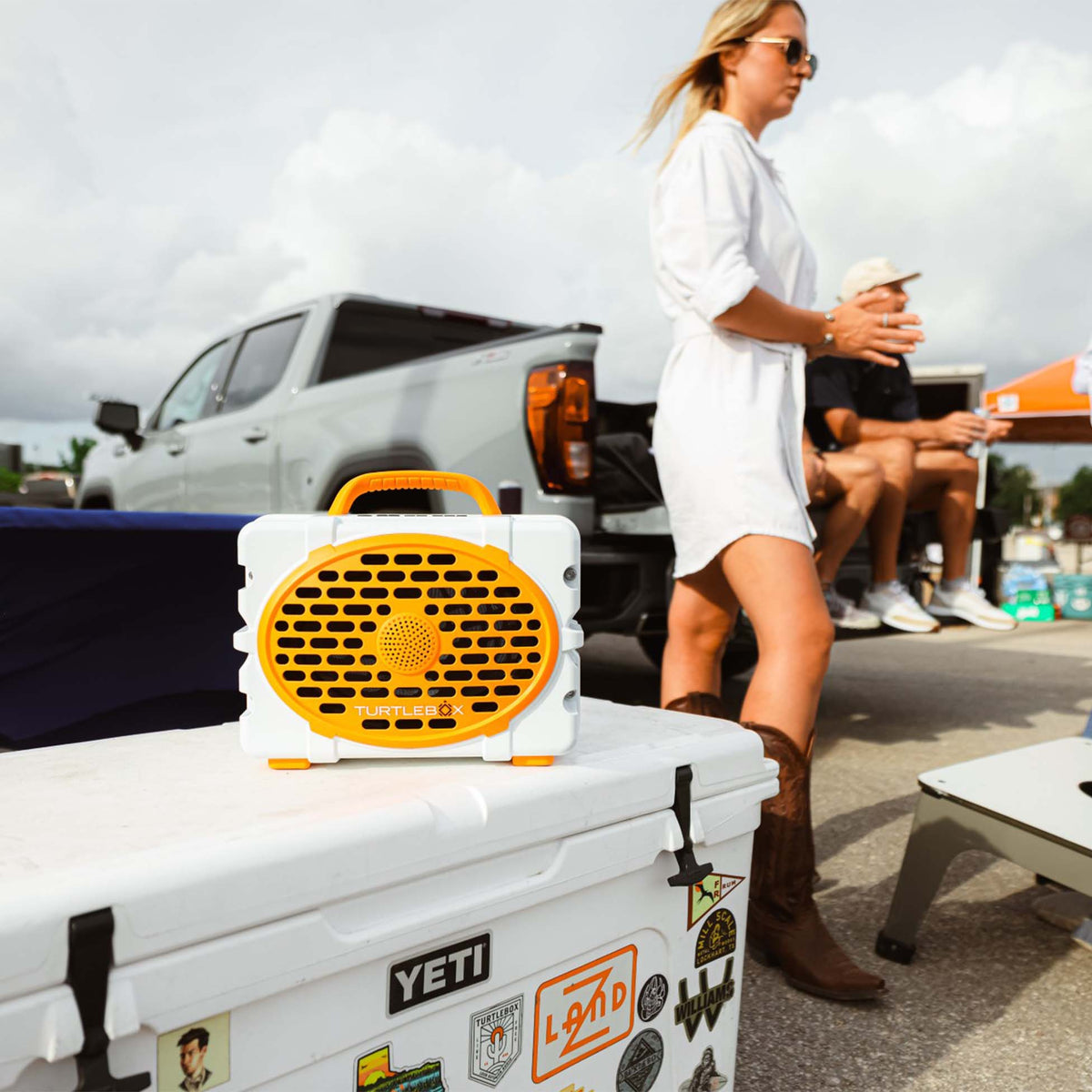 Lifestyle image of TurtleBox Gen 3 UT Orange and White Portable Speaker being used in a tailgating scene