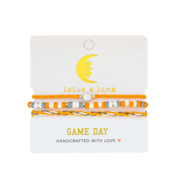Lotus & Luna Game Day bracelet set with orange and white beads, a pearl center, and twisted cord, on branded card packaging.