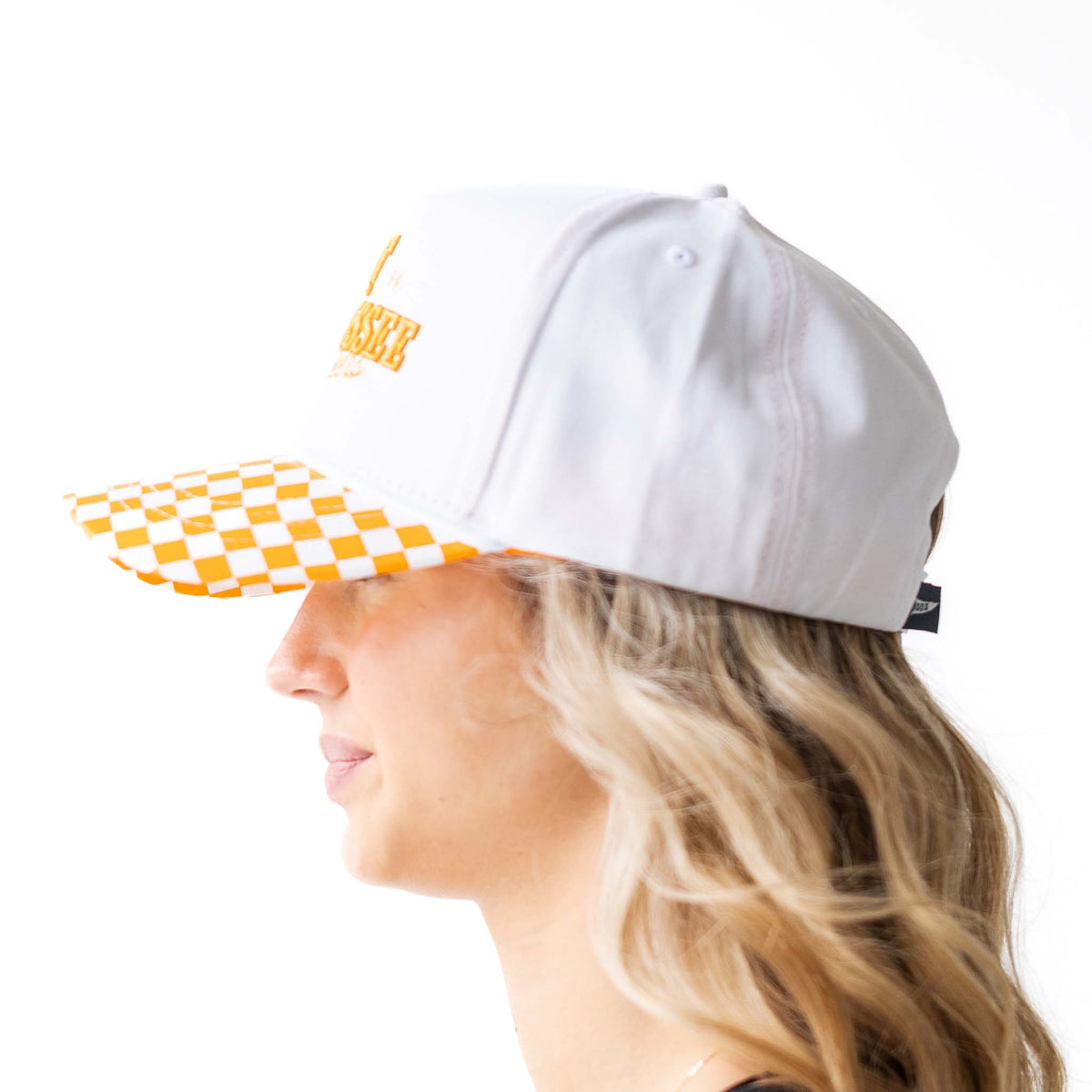 Side profile view of Tennessee Volunteers white hat with orange embroidered logo and checkerboard bill, worn by model.