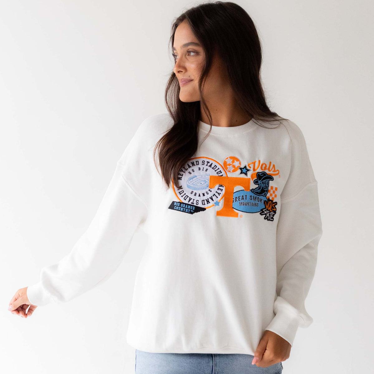 Model wearing white Tennessee Volunteers sweatshirt with bold graphic patches on chest, angled front view.