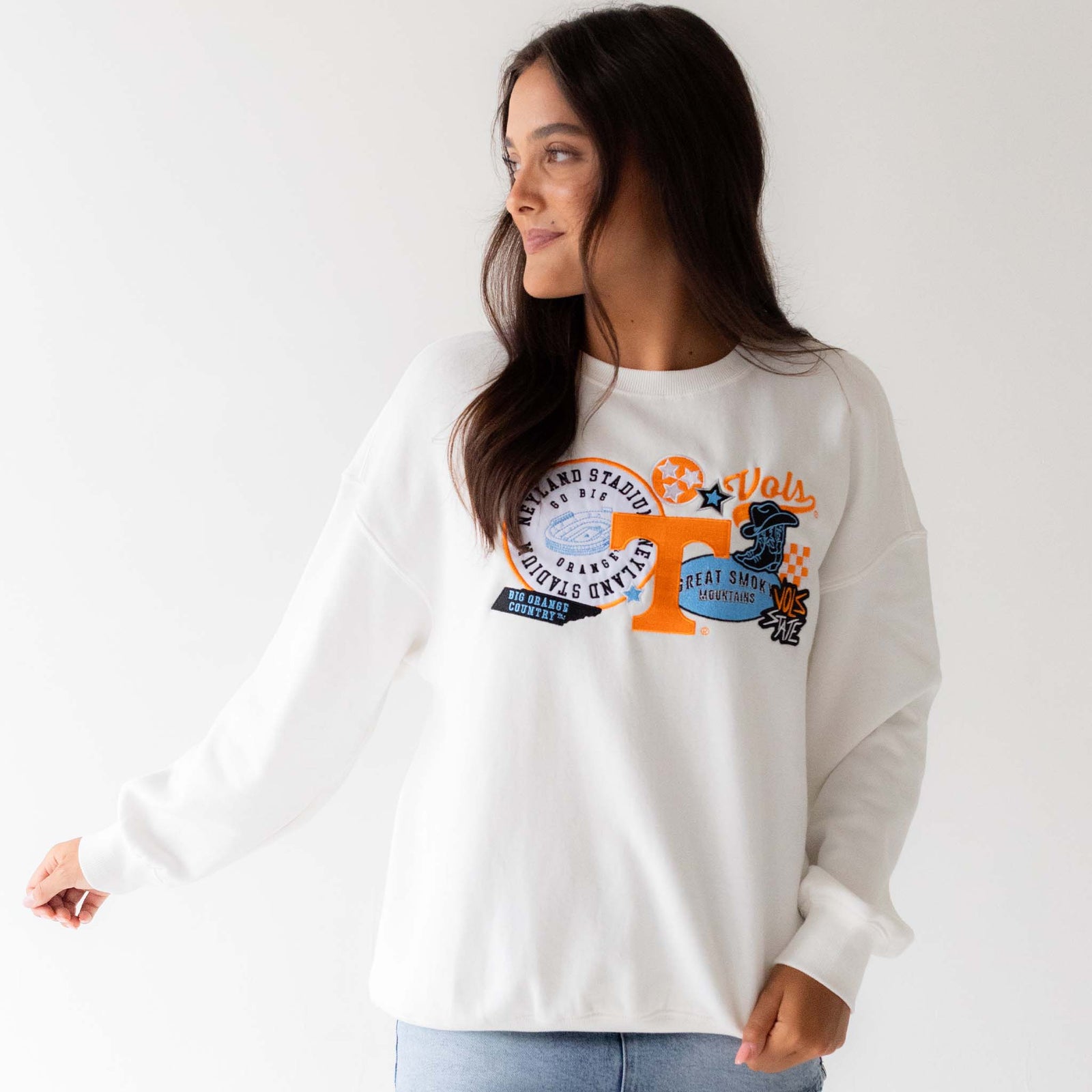 Model wearing white Tennessee Volunteers sweatshirt with bold graphic patches on chest, angled front view.
