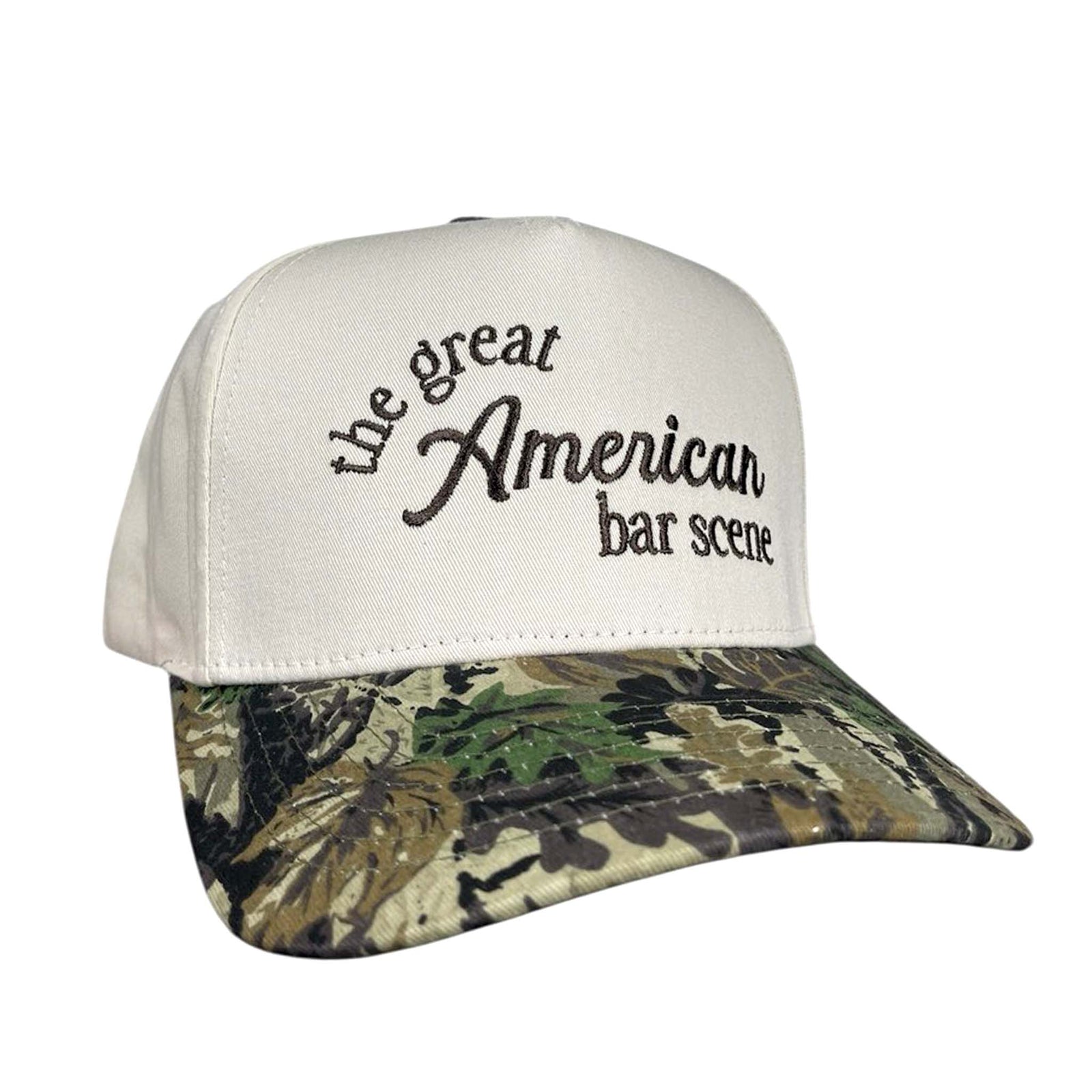 The Happiest trucker hat with cream front, camo print bill, and brown embroidery that reads “the great American bar scene.”