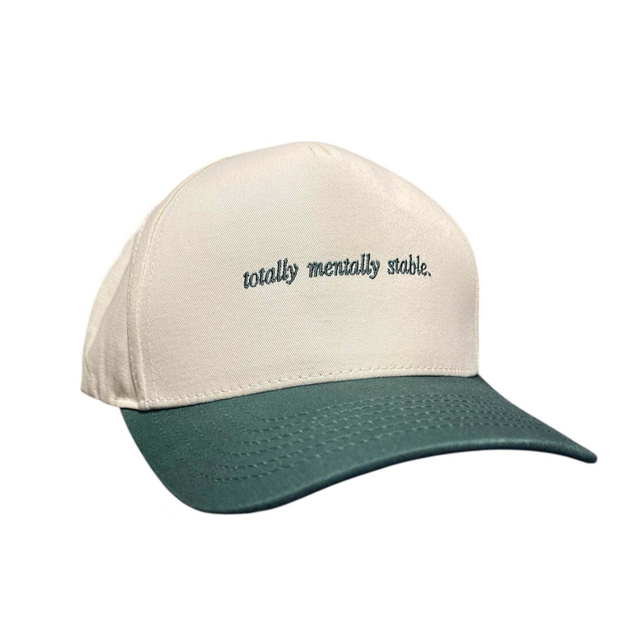 Cream and green trucker hat with embroidered text reading “totally mentally stable.” on the front panel.