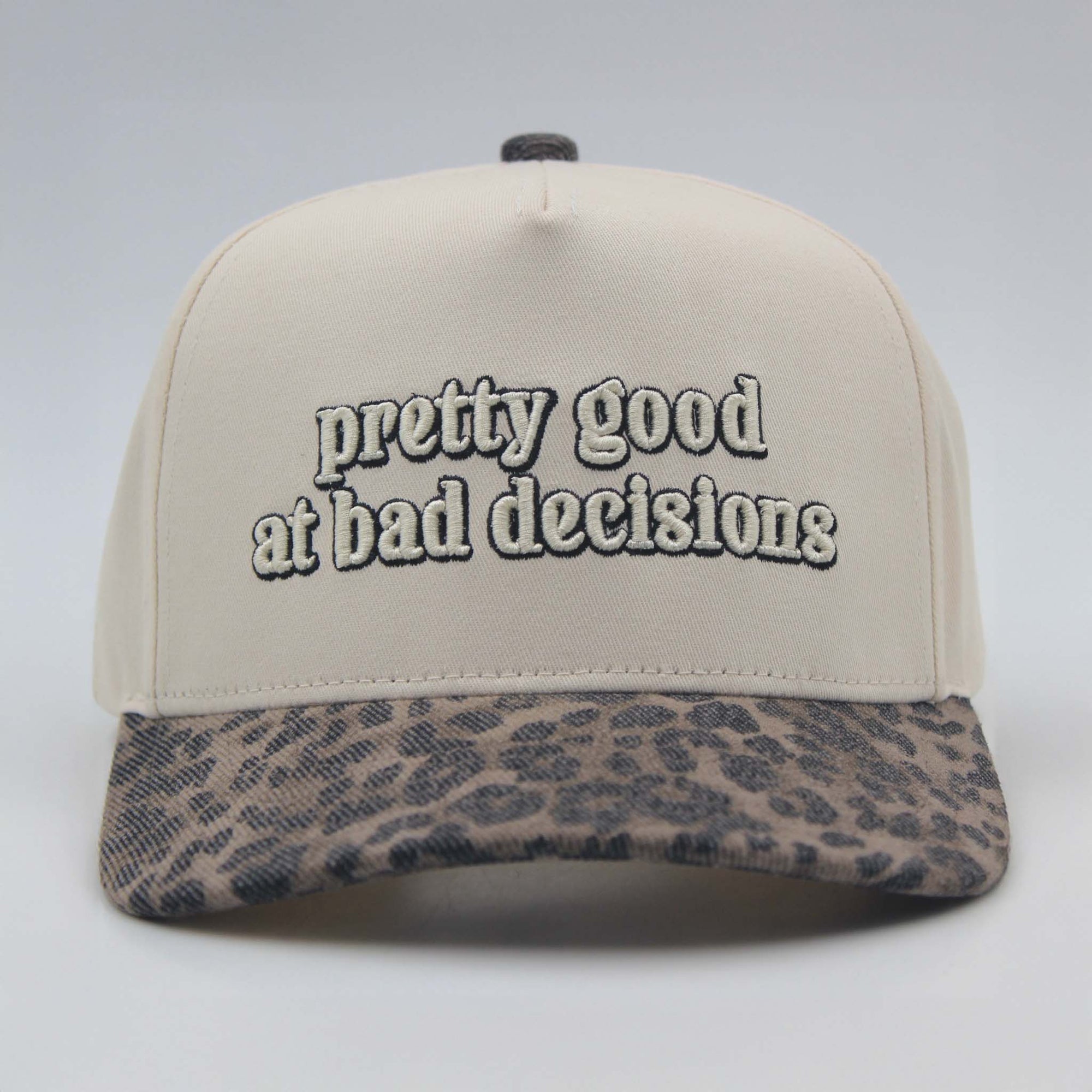 Beige cap with leopard print brim and 'pretty good at bad decisions' text on a light gray background