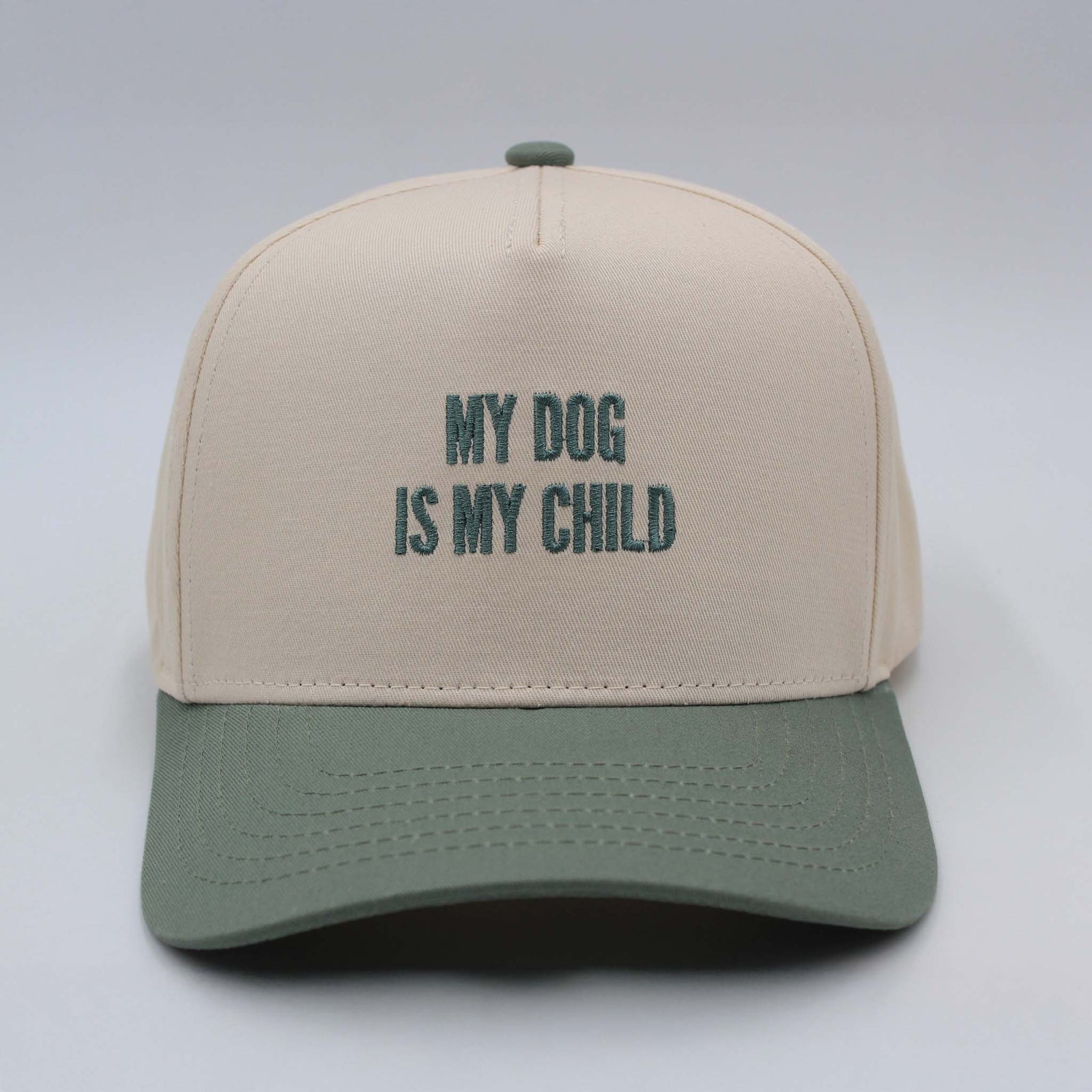 Beige and sage green trucker hat by The Happiest with embroidered text reading ‘My Dog Is My Child’ on the front panel.