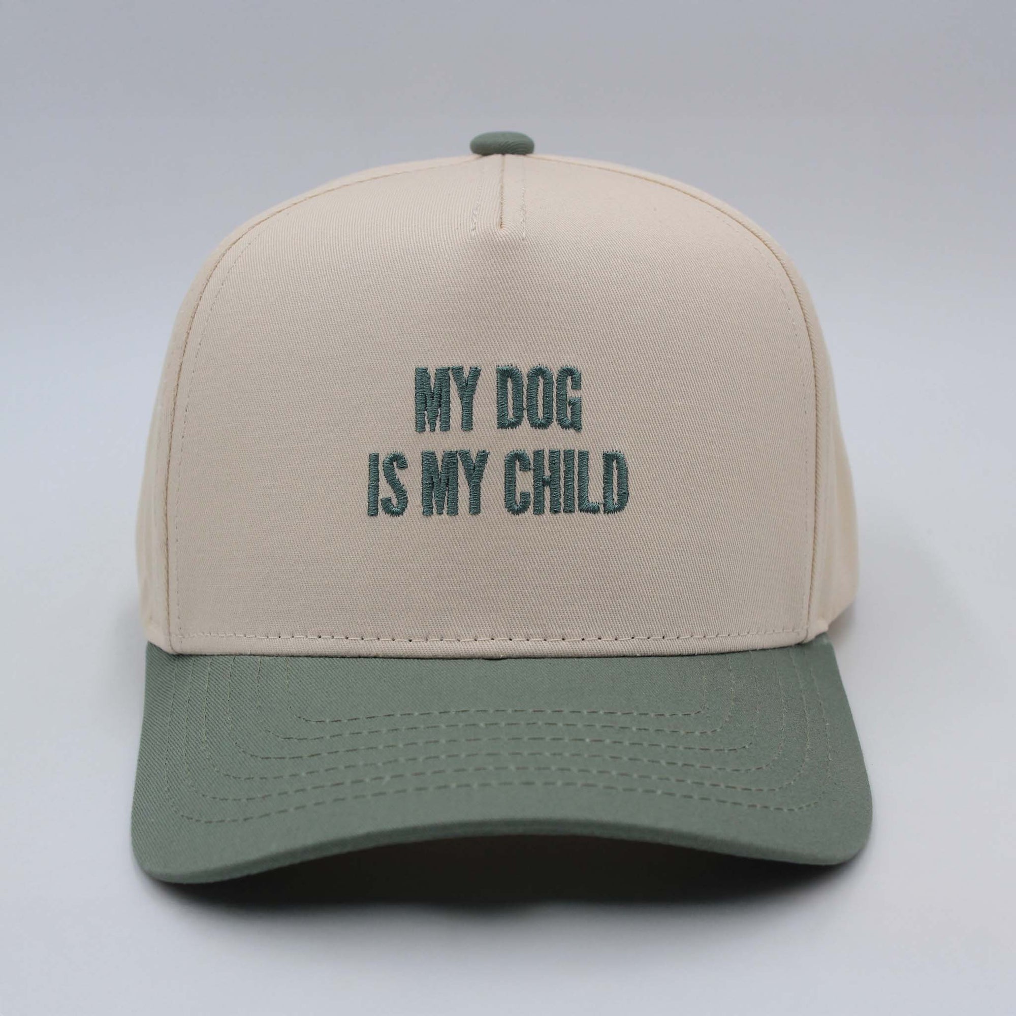 Beige and sage green trucker hat by The Happiest with embroidered text reading ‘My Dog Is My Child’ on the front panel.